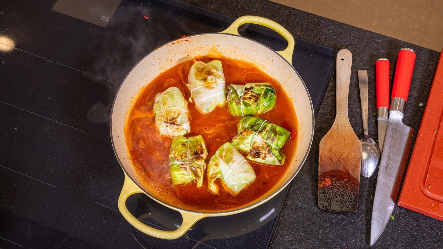 Rezept Kohlrouladen mit Hackfleisch: Die Kohlrouladen in einer roten Soße in einer gelben Pfanne.