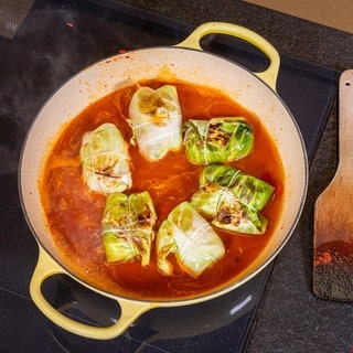 Rezept Kohlrouladen mit Hackfleisch: Die Kohlrouladen in einer roten Soße in einer gelben Pfanne.