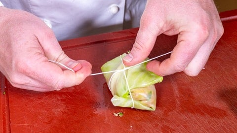 Rezept Kohlrouladen mit Hackfleisch: Der Koch schnürt die Kohlrouladen mit einem Küchengarn zusammen.