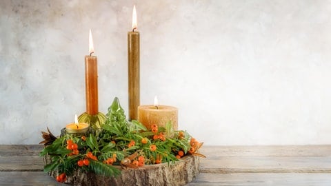 Holz Adventskranz: Vier Kerzen mit grünen Zweigen und orangefarbenen Beeren auf einer Baumscheibe als Advents- und Weihnachtsdekoration.