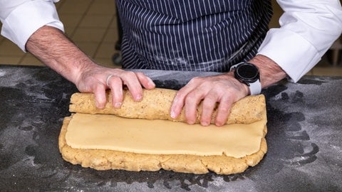 Für den Marzipanstollen den Teig ausrollen und eine  Lage Marzipan auf den ausgerollten Teig legen. Teig und Marzipan werden dann zusammengerollt.