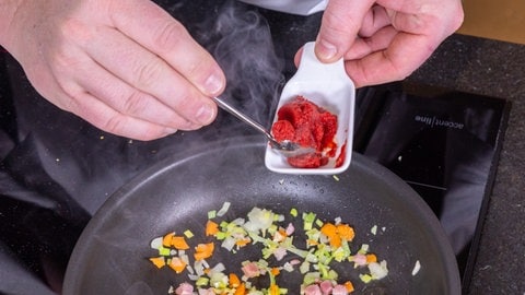 Entenbrust in Orangensauce mit Wirsing: Tomatenmark wird dem Gemüse, das in einer Pfanne schmort, zugegeben.