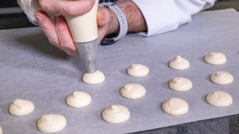 Vanillebrötchen backen: Mit einer Spritztülle wird Teig für mehrere runde Plätzchen auf Backpapier aufdressiert.