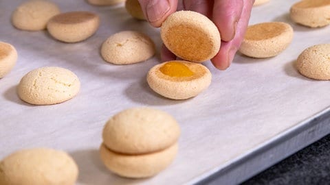 Vanillebrötchen backen: Mehrere mit Aprikosenmarmelade bestrichene Plätzchen werden auf Backpapier zu Doppeldeckern zusammengesetzt.