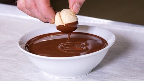 Vanillebrötchen backen: Ein Plätzchen wird in flüssige Schokolade getaucht.