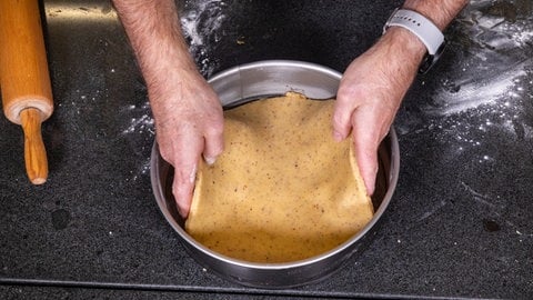 Rezept für Apfelkuchen mit Gitter: Der Boden aus Mürbeteig wird einfach mit zwei Händen angehoben und in die Backform gelegt.