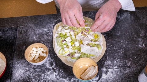 Ein Koch belegt einen original Elsässer Flammkuchen mit Schmand, Lauch und Ziegenkäse.