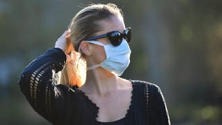 Eine Frau mit Mundschutzmaske traut sich langsam in Corona-Krise Zeiten wieder nach draußen.