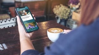 Eine Frau trinkt Kaffee und schaut in die Timeline der SWR Aktuell App