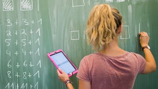 Digitalpakt: Lehrer und Schüler sollen digitale Medien künftig stärker nutzen, das Bild zeigt eine Lehrerin mit einem tablet in der Hand, die an einer Tafel Matheformeln schreibt