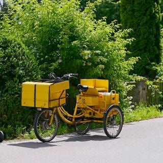 Ein Briefträger der Deutschen Post hat sein Transportrad vor einem Haus abgestellt um die Post an die Haustüre zu bringen.
