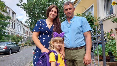 Zusammen mit Mutter Ruslana und deren Partner Andrey freut sich die kleine Viktoria über ihren neuen Schulranzen.