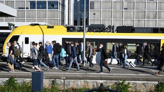 Reisende gehen auf dem Hauptbahnhof Stuttgart auf einem Bahnsteig entlang.