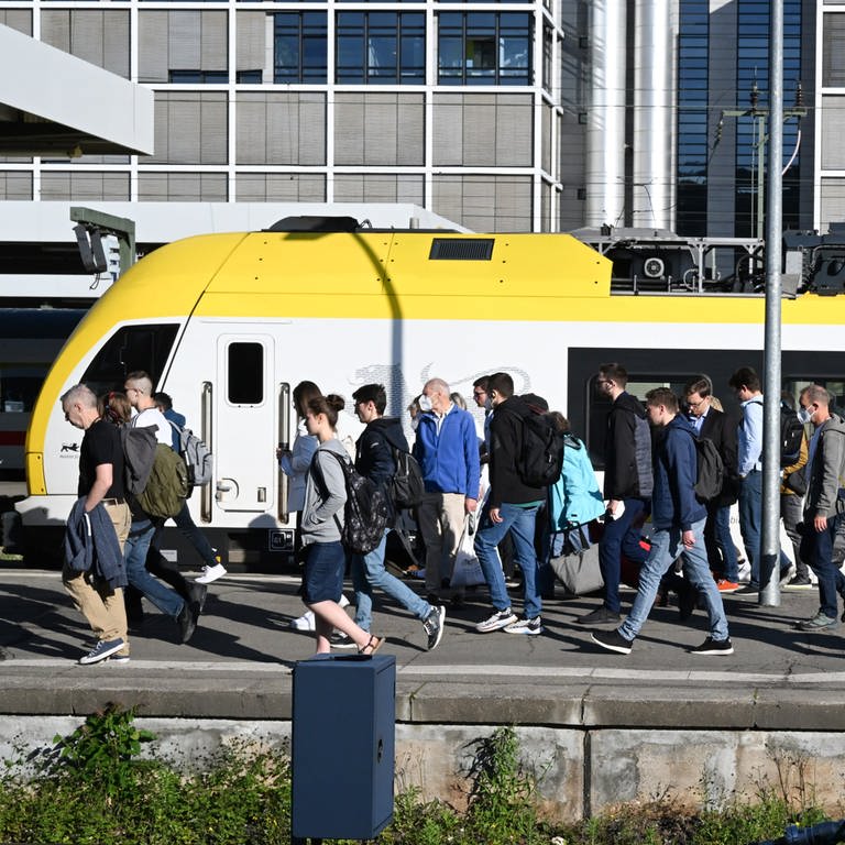 Reisende gehen auf dem Hauptbahnhof Stuttgart auf einem Bahnsteig entlang.