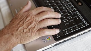Ein älterer Mann tippt auf seinem Laptop. 