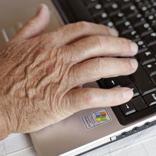Ein älterer Mann tippt auf seinem Laptop. 