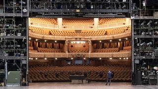 Ein Mitarbeiter der Staatstheater Stuttgart steht auf der Bühne des Opernhauses der Staatstheater Stuttgart, im Hintergrund ist der Zuschauerraum zu sehen. 