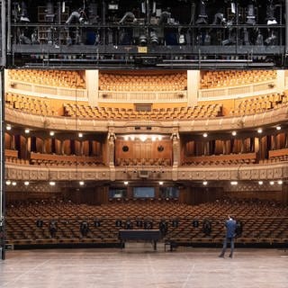 Ein Mitarbeiter der Staatstheater Stuttgart steht auf der Bühne des Opernhauses der Staatstheater Stuttgart, im Hintergrund ist der Zuschauerraum zu sehen. 