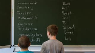 Zwei Schüler einer 1. Klasse stehen vor einer Tafel mit Wörtern in der Gundschule