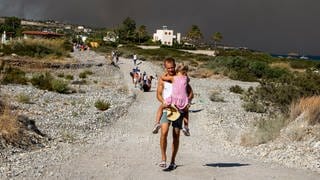 Ein Mann trägt ein Kind, als sie ein Waldbrandgebiet verlassen. Nach der Evakuierung vieler Dörfer und Hotelanlagen wegen großer Waldbrände haben Tausende Menschen auf der griechischen Ferieninsel Rhodos die Nacht im Freien verbracht. 