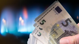 Eine Hand mit Banknoten vor einer Gasflamme.