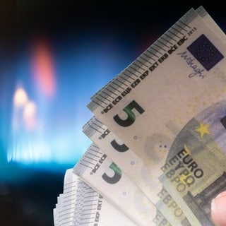 Eine Hand mit Banknoten vor einer Gasflamme.