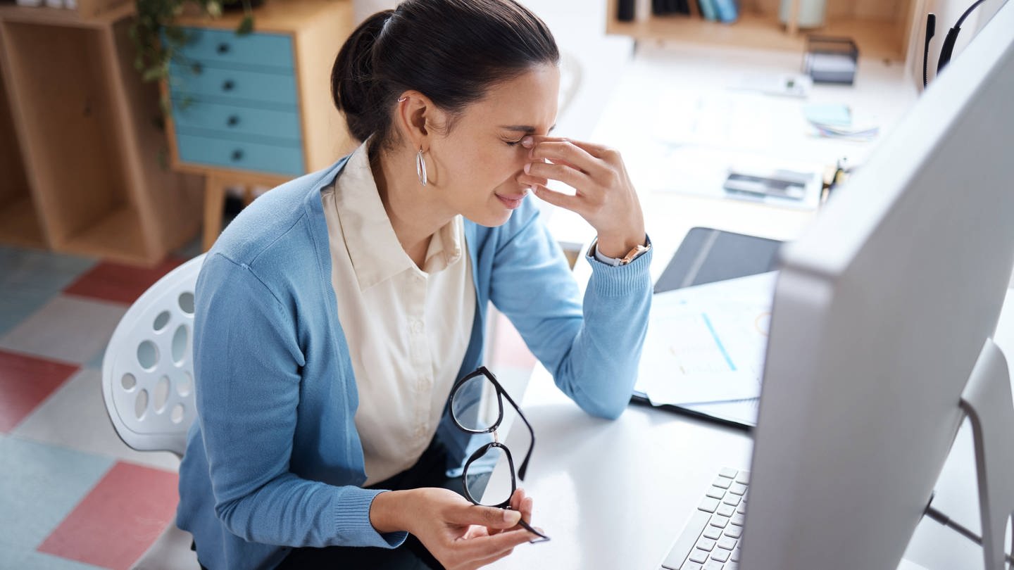 Eine junge Frau sieht gestresst aus, während sie an einem Laptop an ihrem Schreibtisch arbeitet