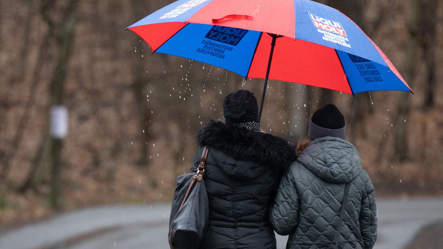 Passanten gehen mit einem Regenschirm auf einer Straße entlang.