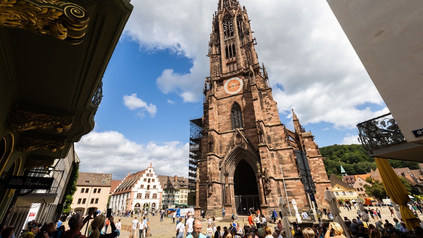 Menschen stehen auf dem Freiburger Münsterplatz vor dem Münster.