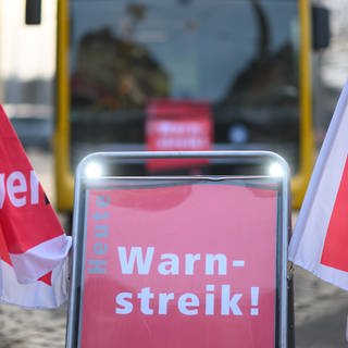 Symbolbild: Ein Schild "Warnstreik" steht vor einem Bus der Dresdner Verkehrsbetriebe (DVB) während des Warnstreiks im öffentlichen Nahverkehr.
