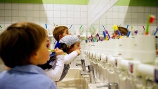 In fünf von ÖkoTest getesten Baby- und Kinderzahnpasten steckt Titandioxid. Der Stoff könnte erbgutschädigend sein. Auf dem Foto putzen Kita-Kinder in einem großen Badezimmer vorm Spiegel ihre Zähne.