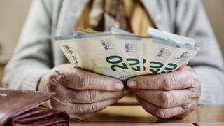 Mehrere 20-Euro-Scheine aufgefächert in den Händen einer Rentnerin.