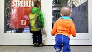 Zwei kleine Kinder stehen vor der Tür eines wegen Streik geschlossenen Kindergartens.