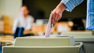 Ein Wahlbrief wird in eine Wahlurne geworfen.