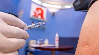 Ein Apotheker hält nah an dem Arm einer Kundin seiner Apotheke eine Spritze mit Grippeschutzimpfstoff. 