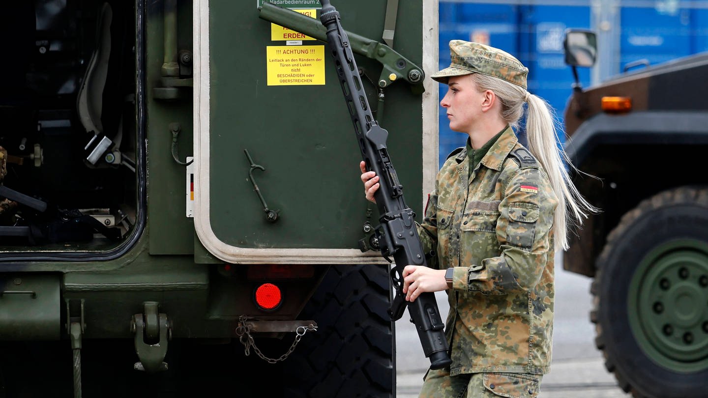 Eine Soldatin trägt ein Maschinengewehr (MG3) vor Militärtechnik (Hummel) in der Systemschau CIR-Fähigkeiten beim Antrittsbesuch von Bundesverteidigungsminister Boris Pistorius (SPD) bei der Cybertruppe