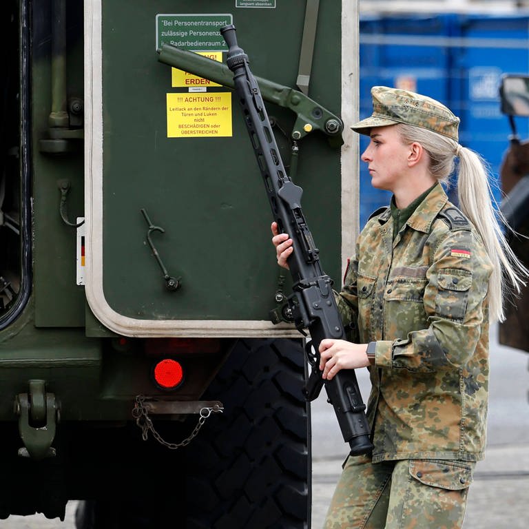 Eine Soldatin trägt ein Maschinengewehr (MG3) vor Militärtechnik (Hummel) in der Systemschau CIR-Fähigkeiten beim Antrittsbesuch von Bundesverteidigungsminister Boris Pistorius (SPD) bei der Cybertruppe