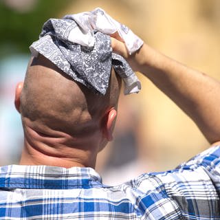 Hitze: Ein schwitzender Mann wischt sich am mit einem Stofftuch über den Kopf