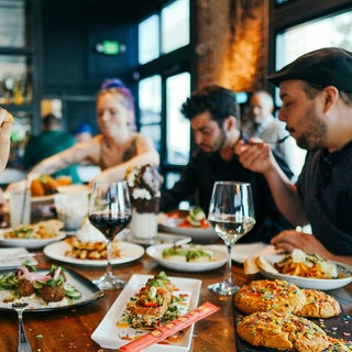 Gäste im Restaurant am Tisch mit vielen gefüllten Tellern: Eine Hauptspeise kostet inzwischen im Vergleich zu kurz vor dem Ukrainekrieg im Schnitt fast ein Viertel des Preises mehr.