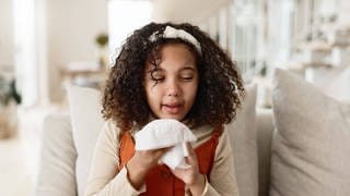 Erkältetes Mädchen sitzt mit Taschentuch in der Hand auf dem Sofa