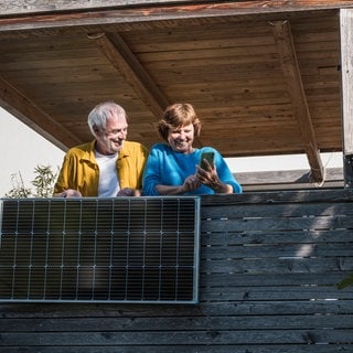 Ein Senior und eine Seniorin mit Smartphone freuen sich über die Leistung ihres Balkonkraftwerks