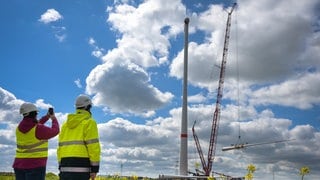 Zur Montage an einem Windrad wird ein Rotorblatt von einem Kran in die Höhe befördert. 