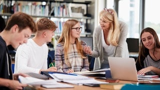 Eine Nachhilfelehrerin unterstützt Schülerinnen und Schüler bei einer Gruppenarbeit