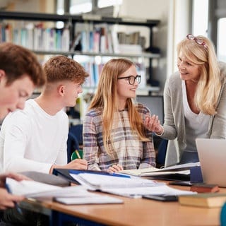 Eine Nachhilfelehrerin unterstützt Schülerinnen und Schüler bei einer Gruppenarbeit