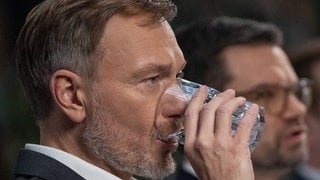 Christian Lindner trinkt Wasser aus einem Glas. Im Hintergrund spricht Marco Buschmann