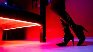 Eine Prostituierte steht an einem rot beleuchteten Bett in einem Studio.