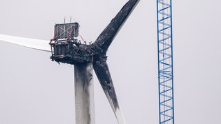 Ein Kran ist an einem Windrad aufgebaut, das von einem Brand zerstört wurde. Brände an Windrädern belasten die Umwelt und verursachen hohe finanzielle Schäden