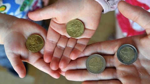 Drei Kinderhände halten 2-Euro und 50-Centmünzen ins Bild