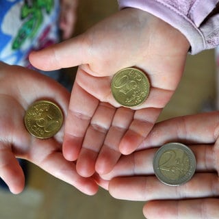 Drei Kinderhände halten 2-Euro und 50-Centmünzen ins Bild