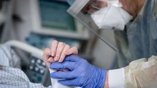 Ein Intensivpfleger hält die Hand eines Patienten beim Blutabnehmen